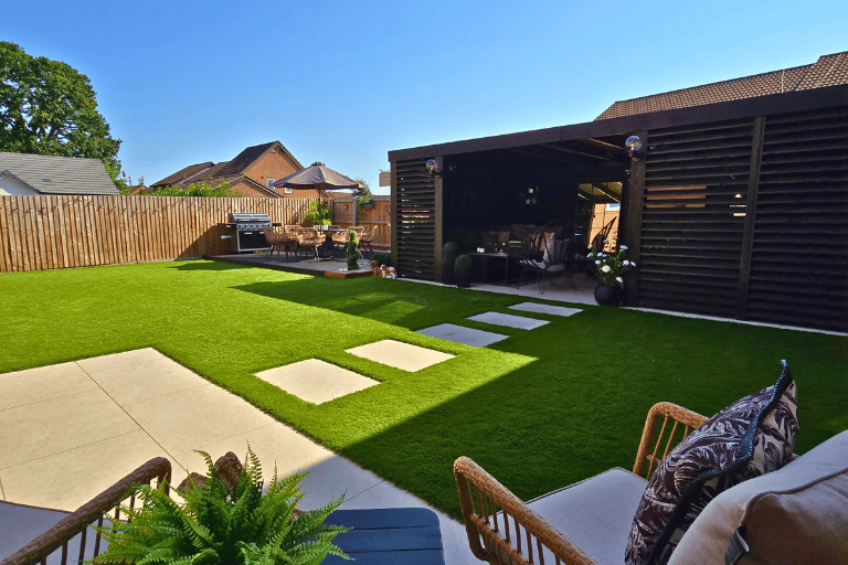 Spacious garden with artificial lawn, stepping stones, patio seating, and outdoor kitchen.